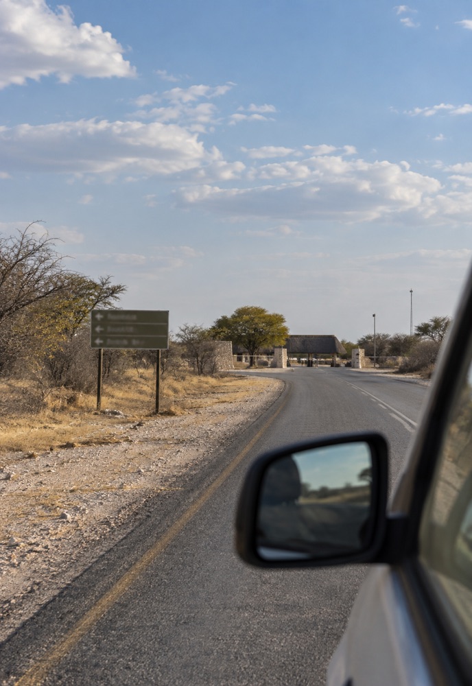 Fahrzeug auf der Zufahrt zu einem Etosha-Eingang mit Wegweiser